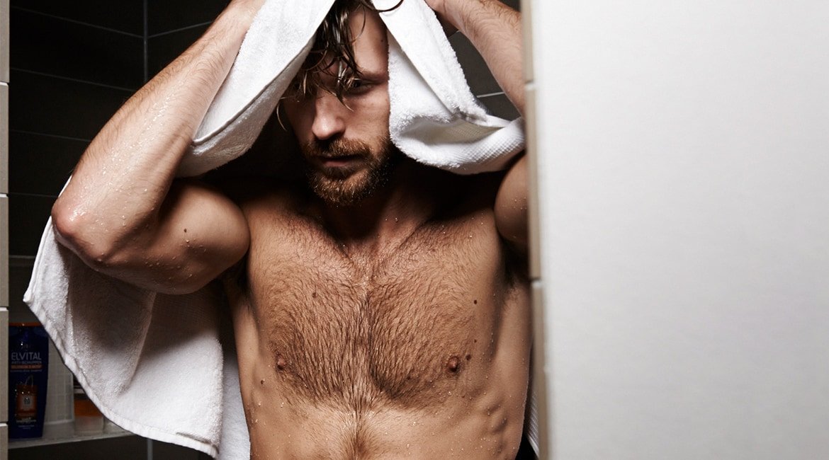 Ein Mann mit freiem Oberkörper trocknet sich die Haare mit einem Handtuch